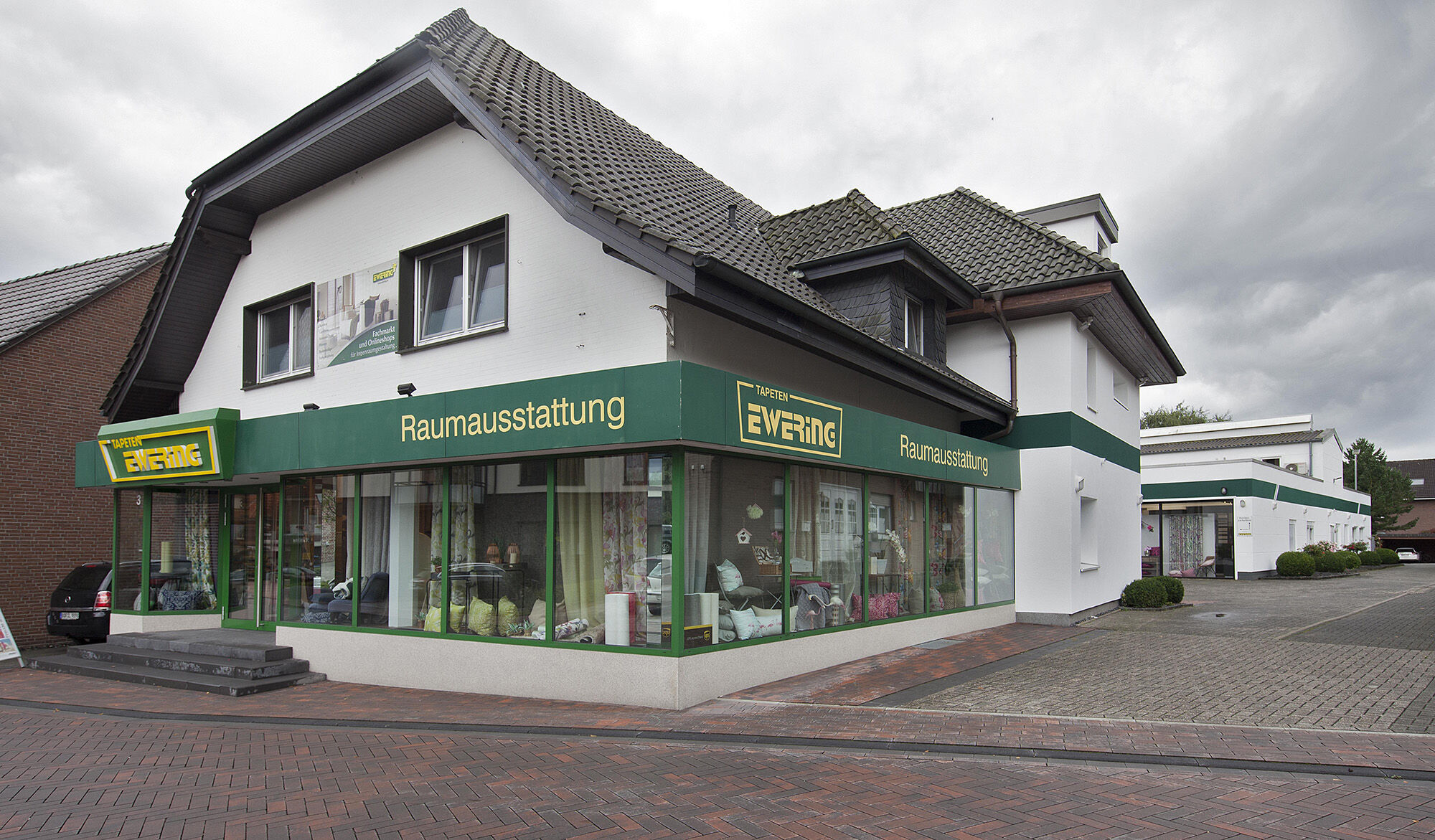 Außenansicht vom Ewering Raumdesign Fachmarkt Gebäude in Reken mit großzügiger Fensterfront und Firmenlogo – einladender Eingang für individuelle Raumgestaltung und hochwertige Wohnaccessoires.