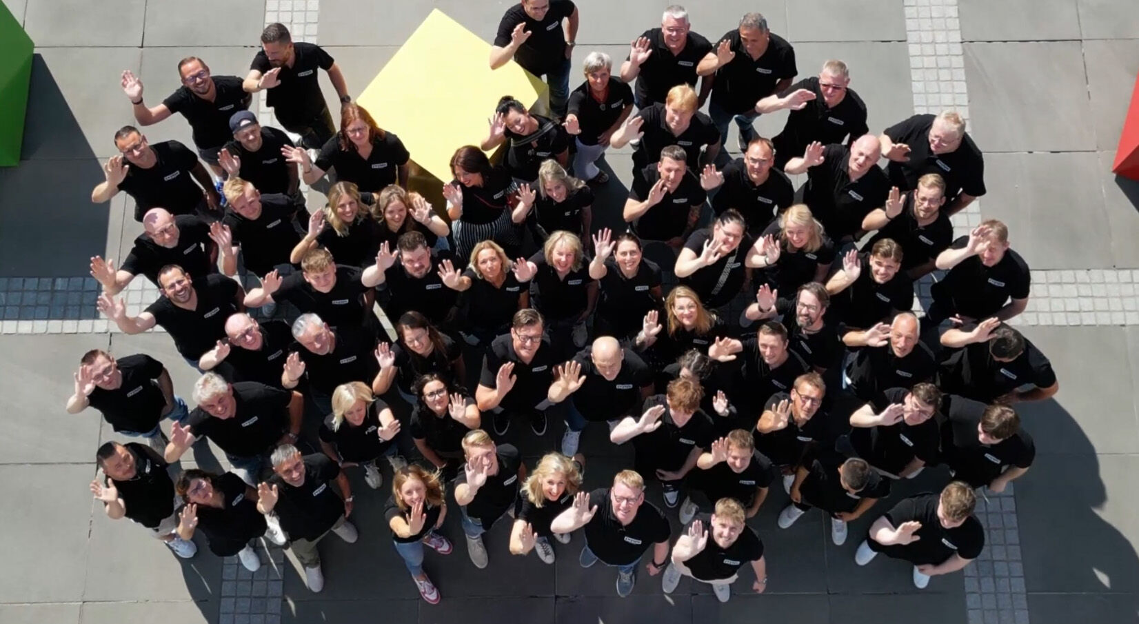 Ewering Gruppenbild von oben mit winkenden Mitarbeitern in schwarzen Ewering T-Shirts