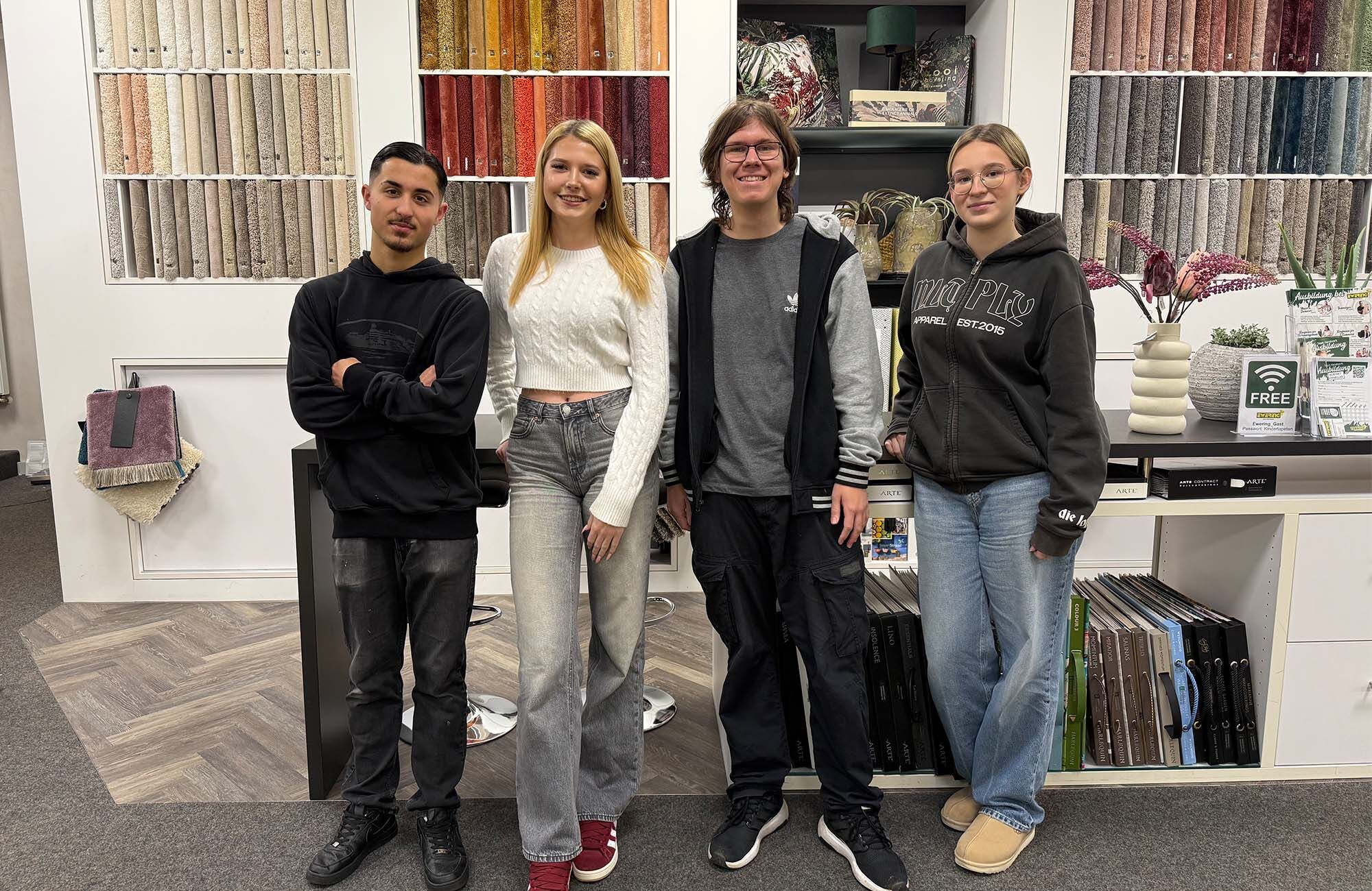 gruppenbild von den aktuellen Azubis 2026 bei Ewering. Die Azubis stehen vor der Teppichmusterwand im fachmarkt nebeneinander.