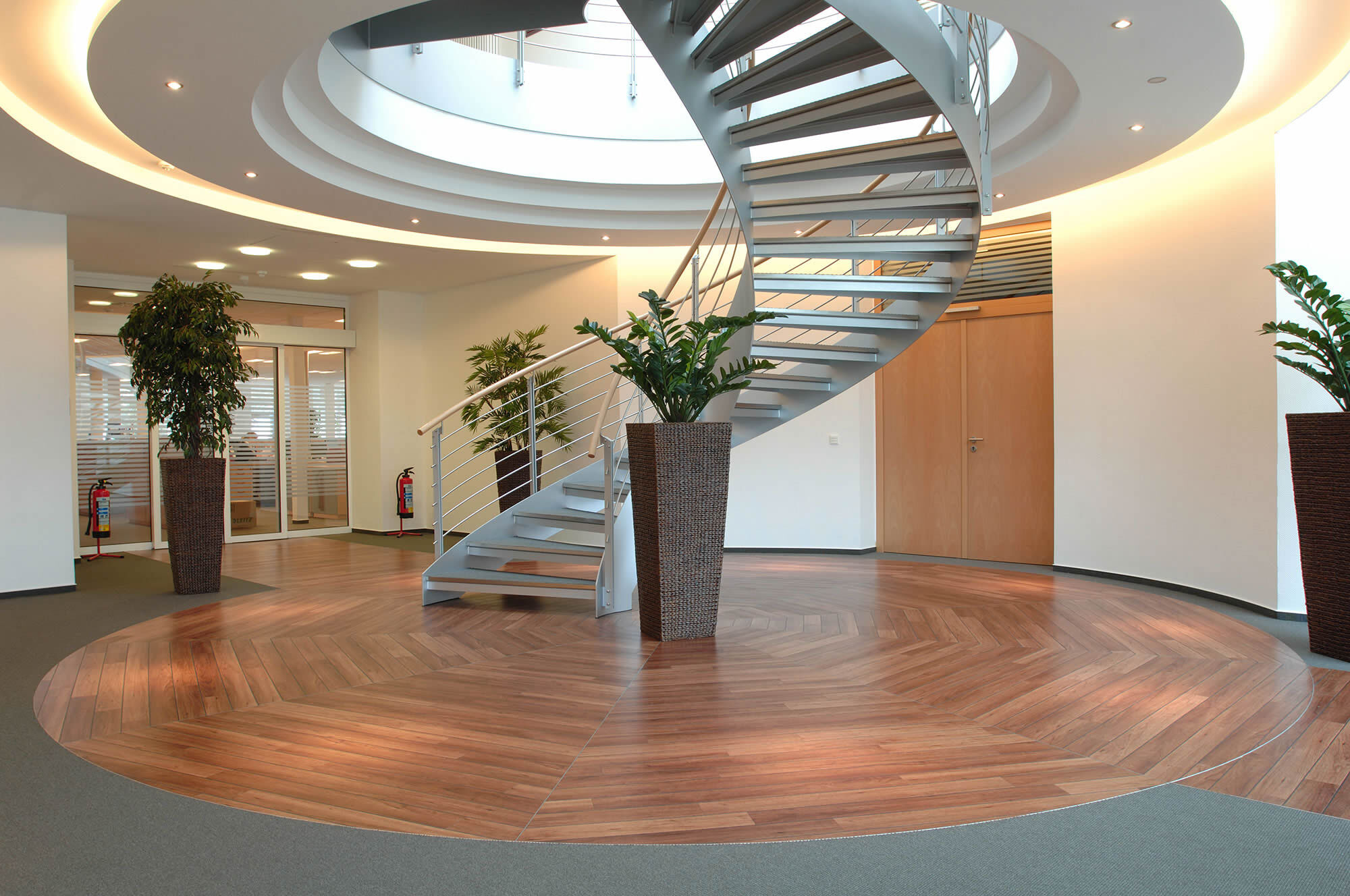 Modernes Treppenfoyer mit rundem Grundriss und hochwertig verlegtem Amtico Designboden in Holzoptik. Das Bild zeigt sauber ausgeführte Bodenbelagsarbeiten in einem repräsentativen Eingangsbereich.