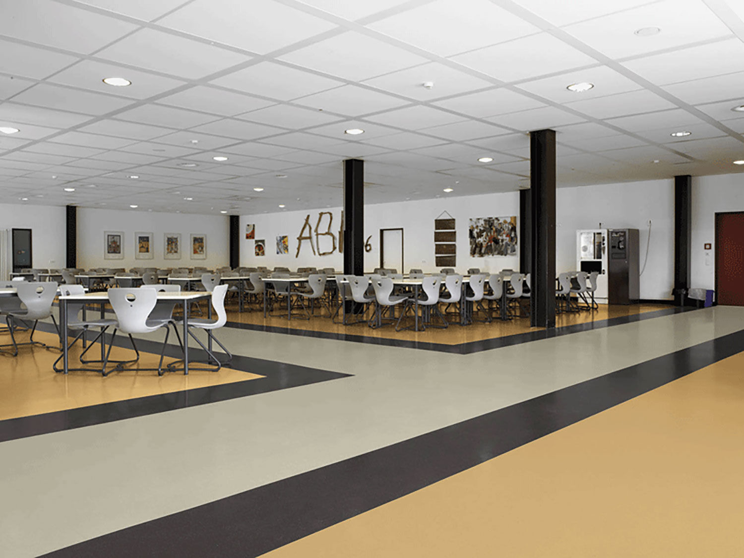 Großer Gemeinschaftsraum mit hochwertig verlegtem Kautschukboden in heller und dunkler Flächengestaltung. Das Bild zeigt sauber ausgeführte Bodenbelagsarbeiten in einem stark genutzten Innenraum mit klarer, robuster und gepflegter Raumwirkung.