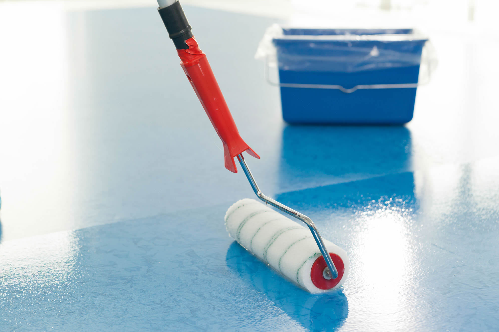 Detailansicht einer Bodenbeschichtung mit Dr. Schutz im Rollerauftrag auf blauer Bodenfläche. Das Bild zeigt präzise ausgeführte Bodenbelagsarbeiten bei der Beschichtung und Aufarbeitung eines Bodenbelags.