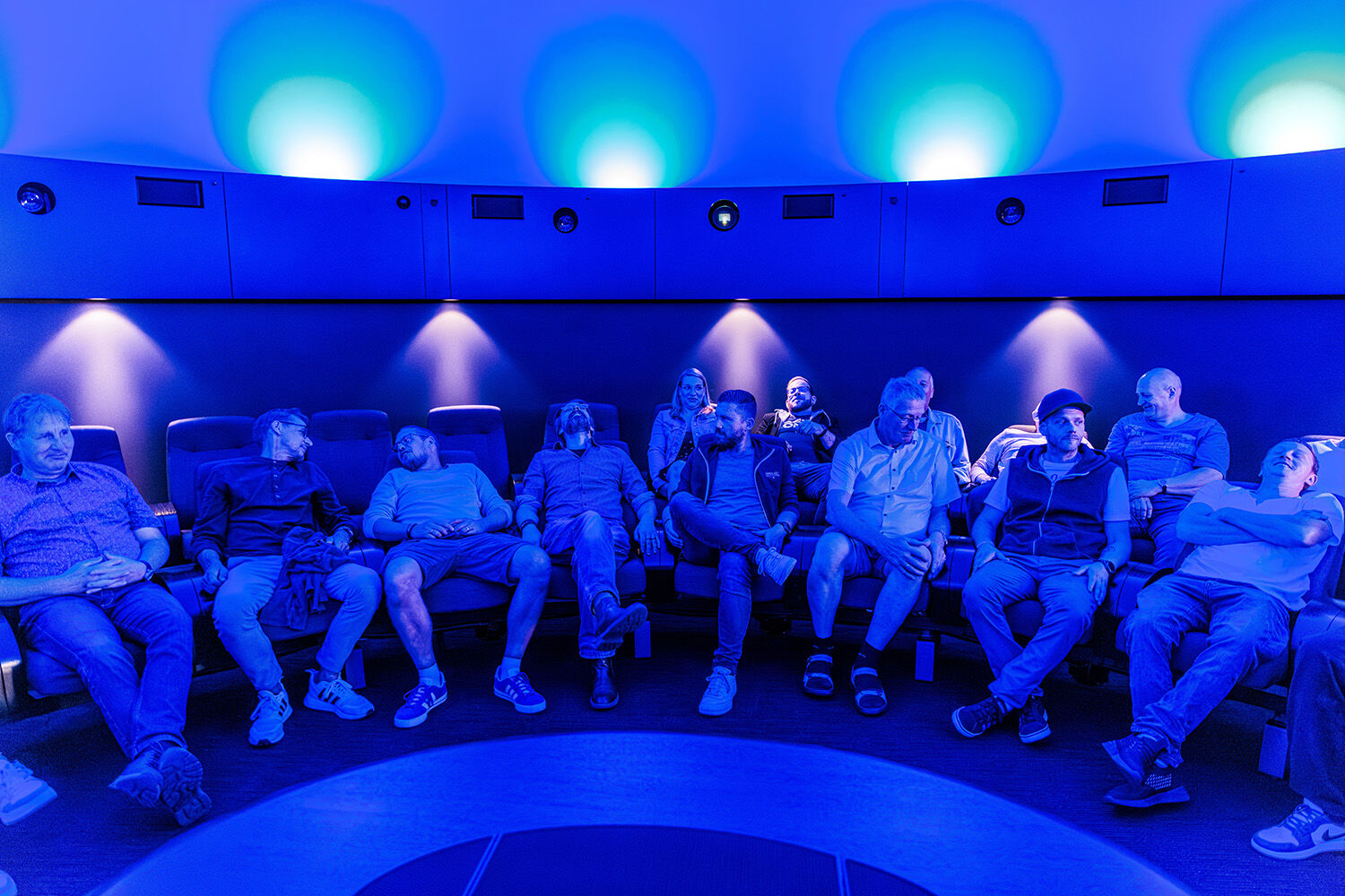 Mehrere Mitarbeitende und Gäste sitzen beim Ewering Sommerfest 2025 in einem blau beleuchteten Veranstaltungsraum in einer Sitzreihe