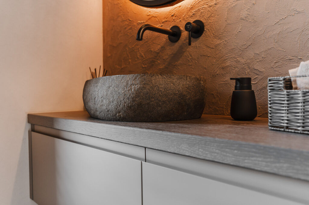 Detailaufnahme eines modernen Waschplatzes mit Frescolori Wandgestaltung, dunklem Steinbecken, schwarzer Armatur, Hängeleuchte und schwebendem Waschtisch.