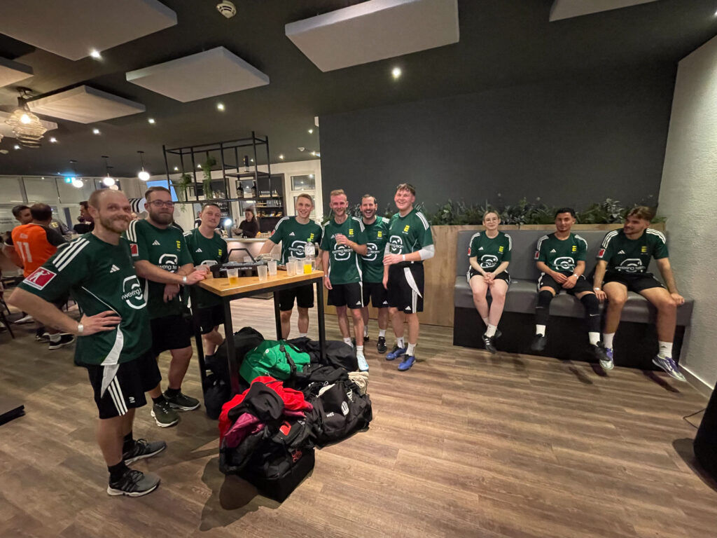 Gruppenbild des Ewering Teams in grünen Trikots nach dem Firmenfußballturnier in einer Lounge- und Barbereich