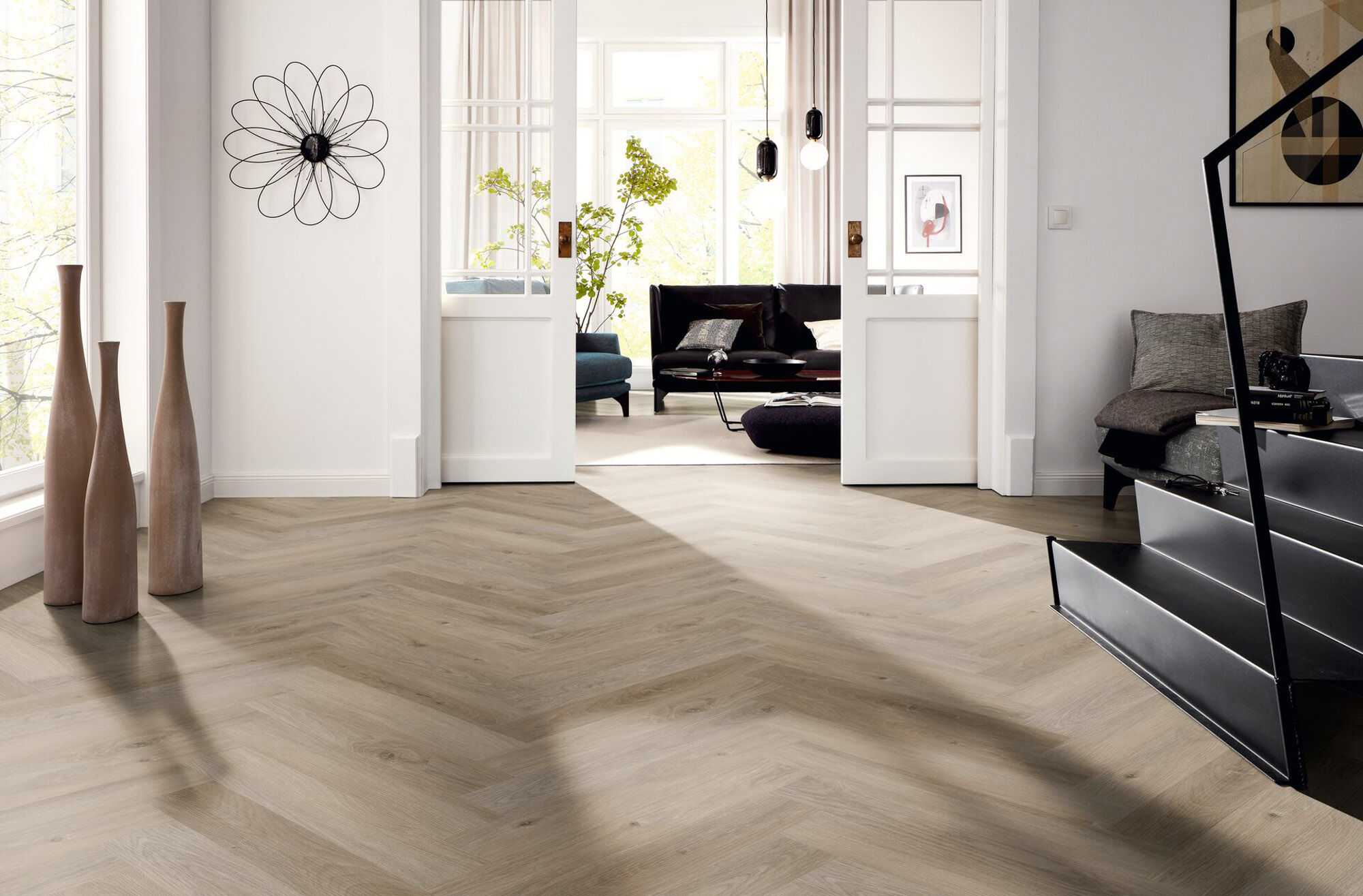 Heller Wohnbereich mit Designbelag in Holzoptik, Fischgrätverlegung, weißer Doppeltür und dunkler Treppe