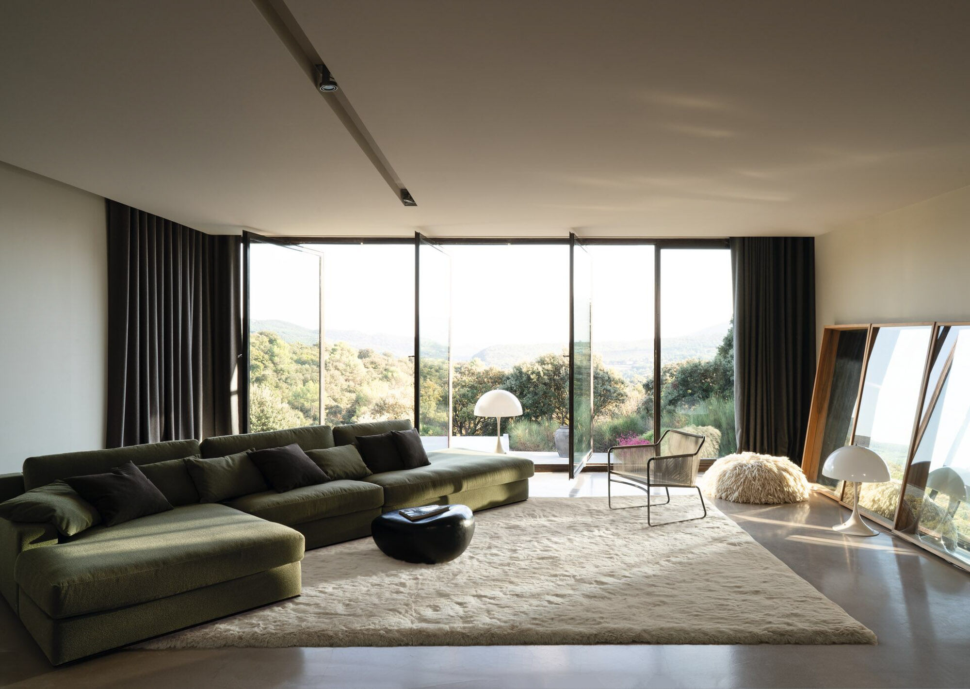 Modernes Wohnzimmer mit großformatigem hellen Hochflor-Teppich, grünem Ecksofa, bodentiefer Fensterfront und dunklen Gardinen