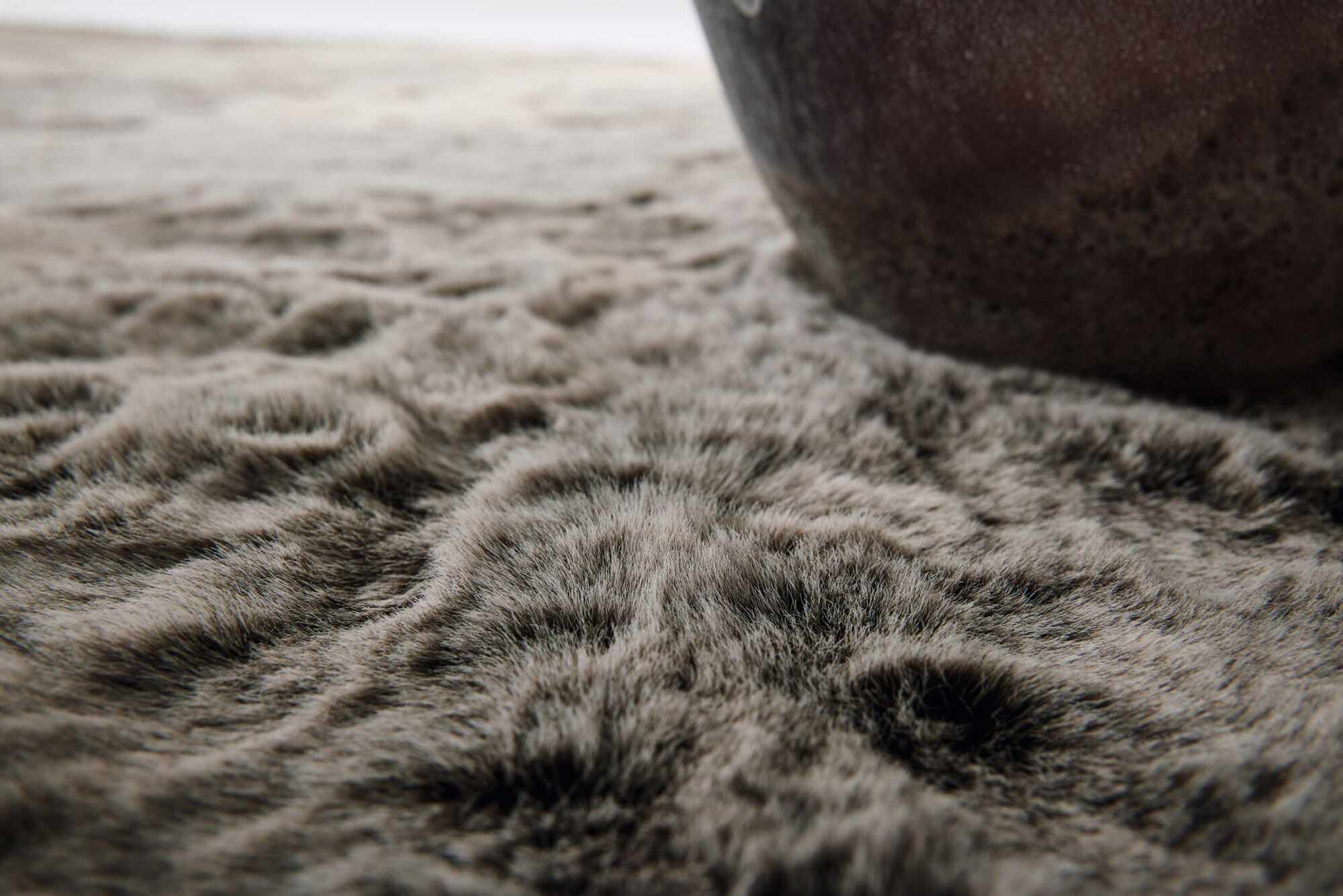 Detailaufnahme eines graubraunen Hochflor-Teppichs mit dichter Florstruktur, weicher Felloptik und changierender Oberfläche
