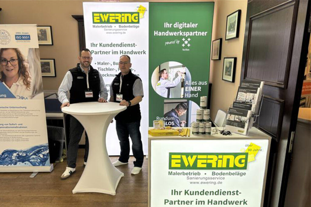 Ewering-Messestand beim VDIV 2025 in Berlin mit zwei Mitarbeitern, Roll-ups, Infomaterial und Kundendienst-Angeboten für das Handwerk