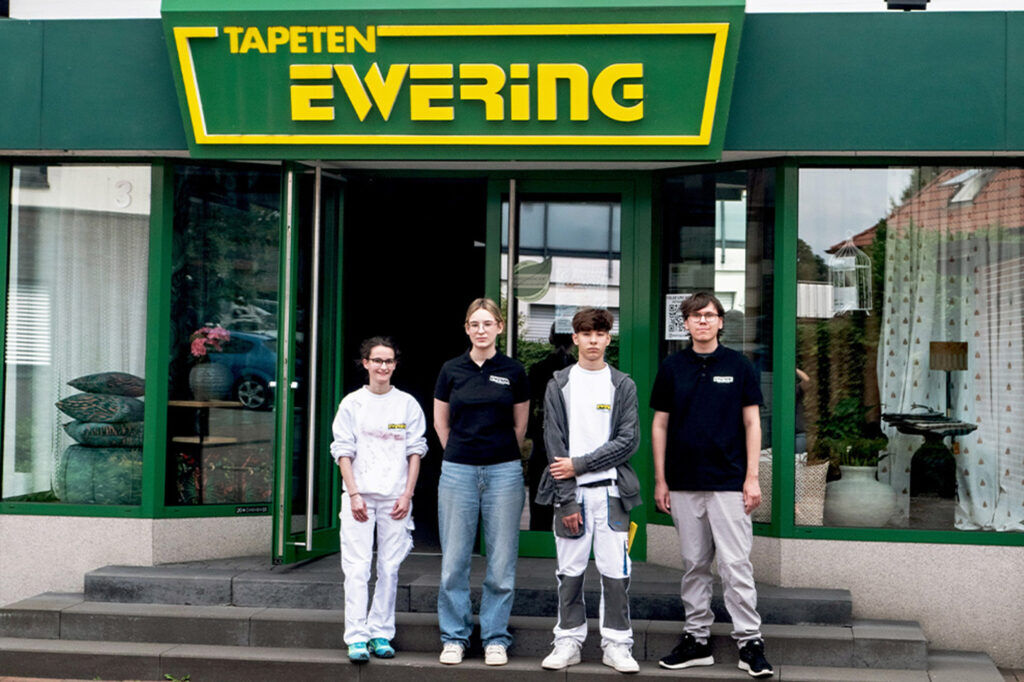 Gruppenbild vor dem Fachmarkt von den vier neuen Azubis bei ewering 2025. Sie sind alle in einer Reihe aufgestellt.