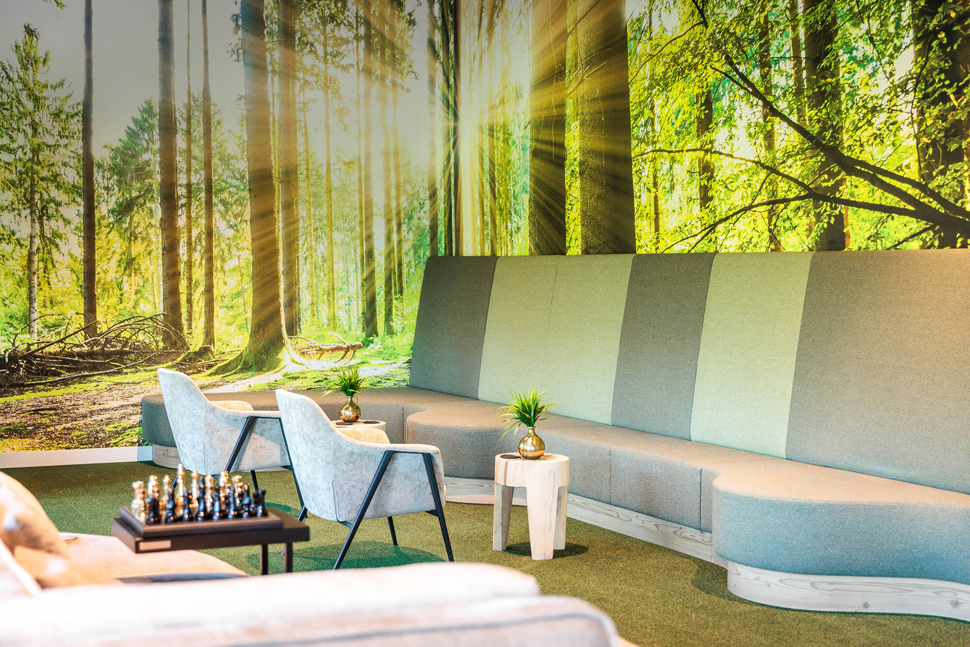 Nahaufnahme Wartebereich mit Schachtisch, Polstersesseln und Wald-Fototapete im Hintergrund