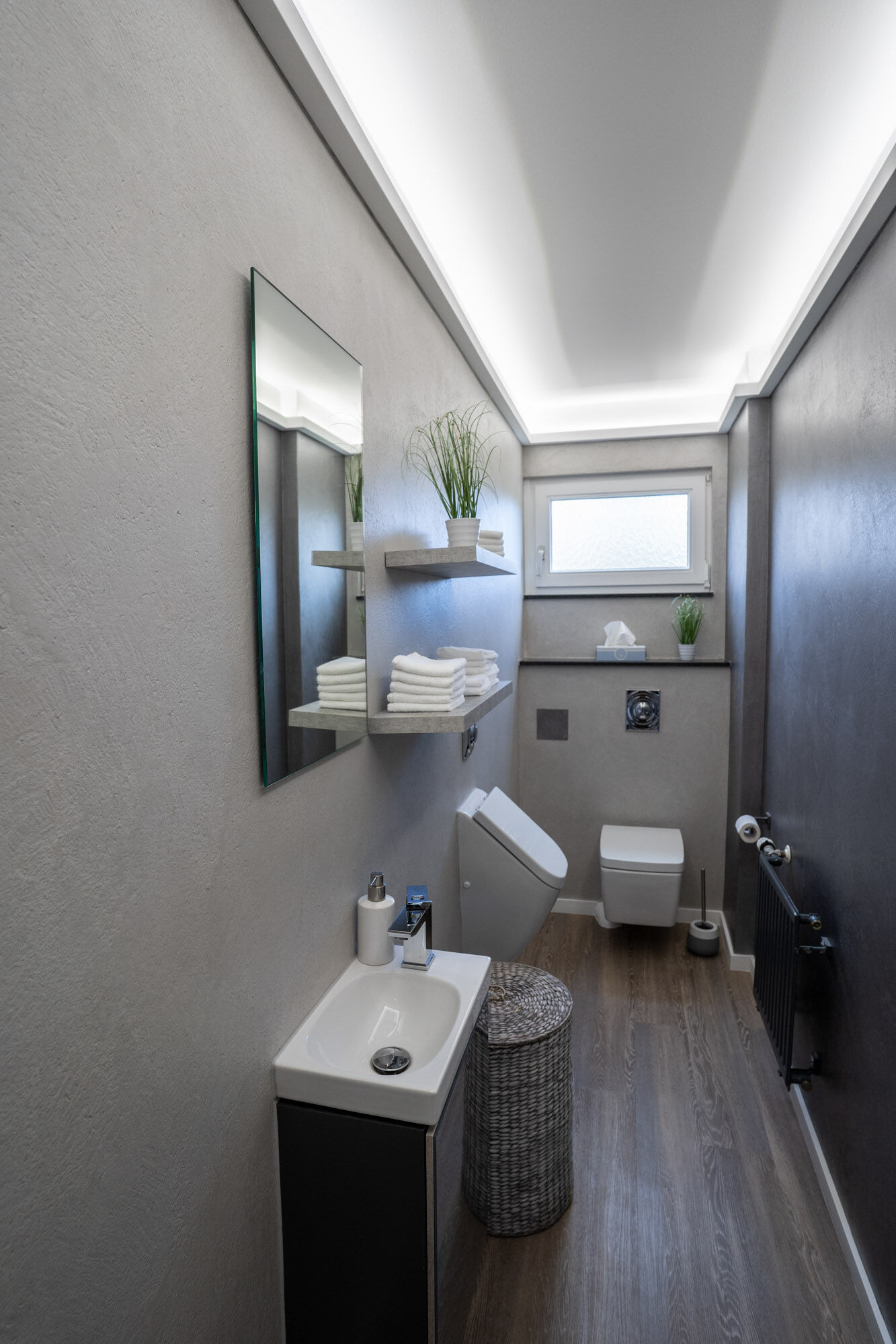Gästebad mit grauer Frescolori-Wand, LED-Spiegel und Holzboden – Exklusives Frescolori-Badezimmer