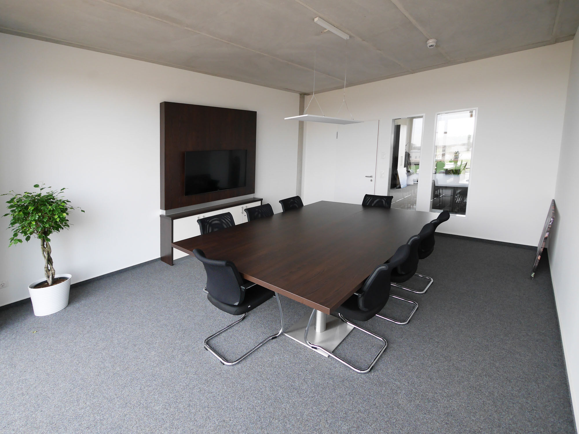 Konferenzraum mit braunem Teppichboden, dunkelbraunem Konferenztisch und TV-Wand – IDPM Gebäude B