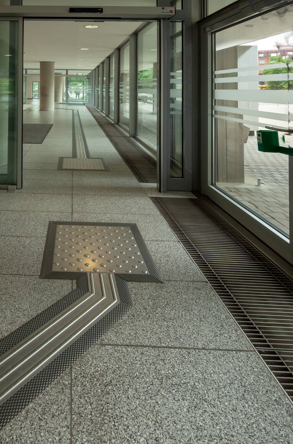 Aufmerksamkeitsfeld mit Noppen und Leitstreifen eines Blindenleitsystems vor einer automatischen Tür.