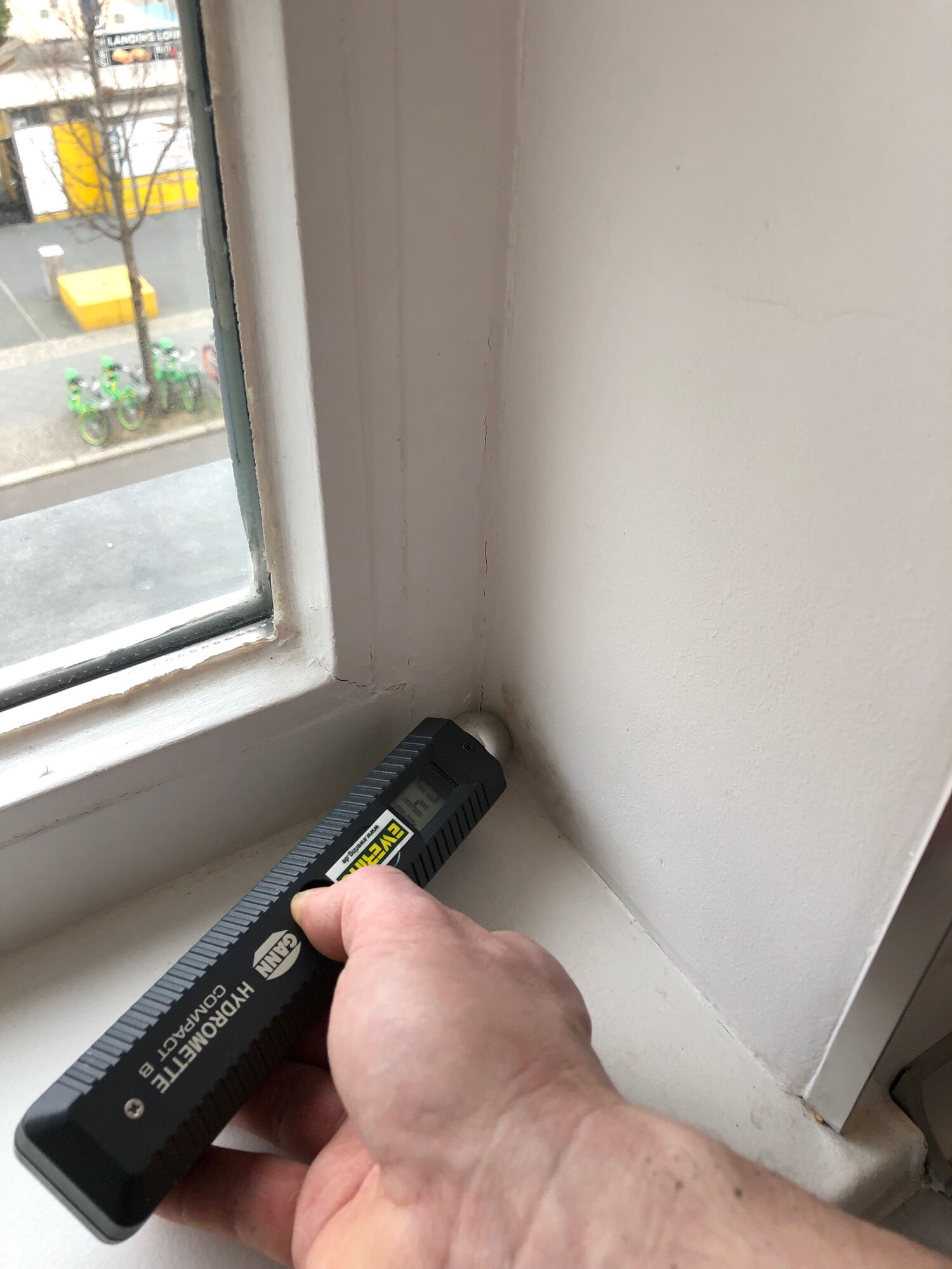 Hand mit Hydromette misst Feuchte an Fensterleibung im Erkerbereich - Schimmelsanierung
