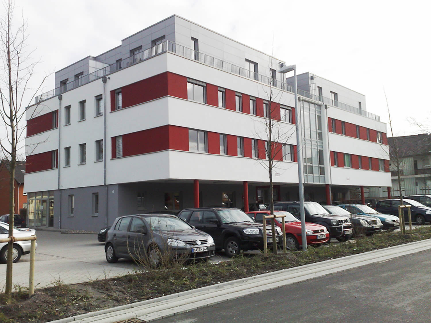 Mehrfamilienhaus mit roter Fassade, weißen und grauen Sockelflächen, Ärztehaus Mülheim