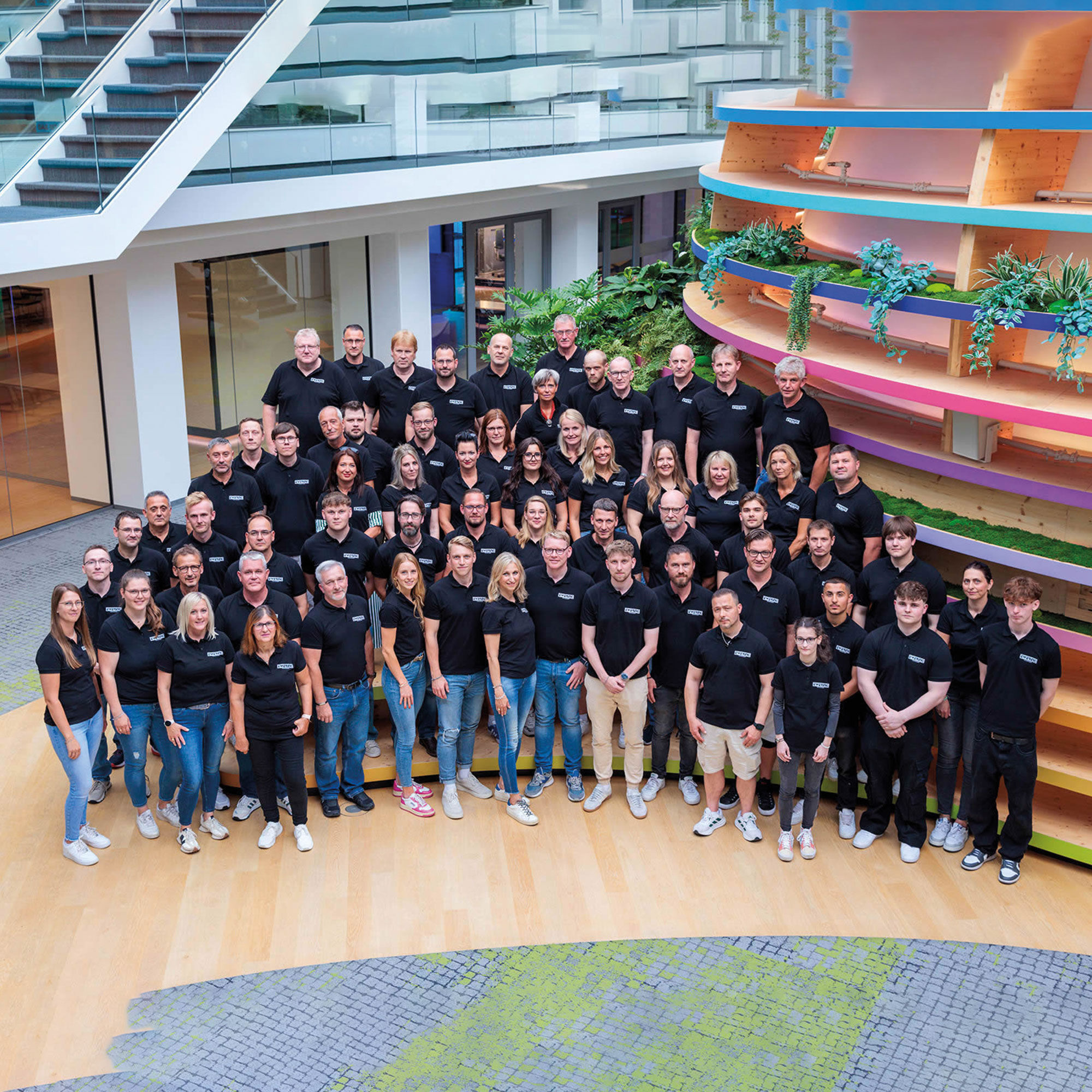 Großes EWERING Team bei einem Gruppenfoto in einem modernen Atrium mit Treppe, Holzflächen und bepflanzter Innenarchitektur